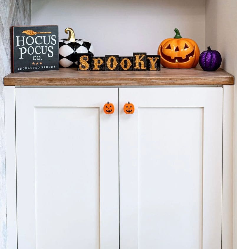 kitchen knobs that are black and orange jack-o-lanterns on white kitchen cabinets