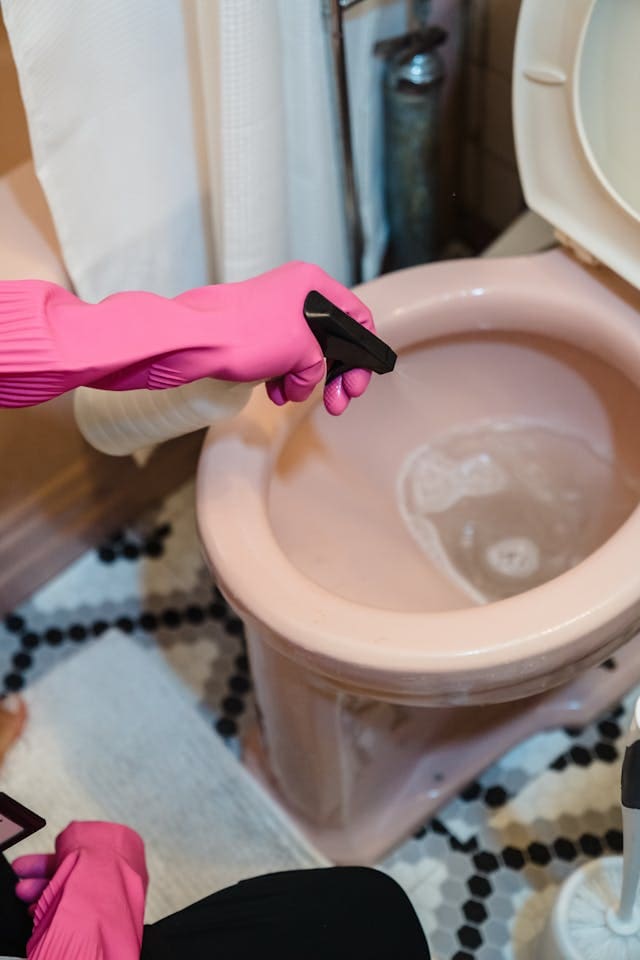 woman using a spray bottle to clean a pink toilet 