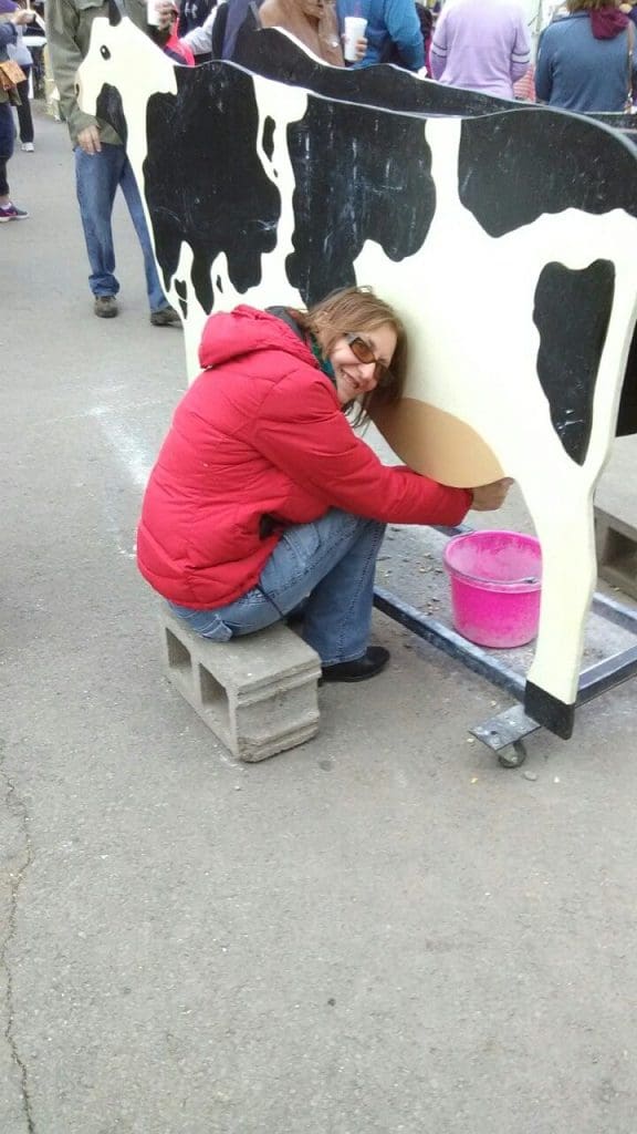 wooden cutout of a cow with woman posing for a photo at a farmstand