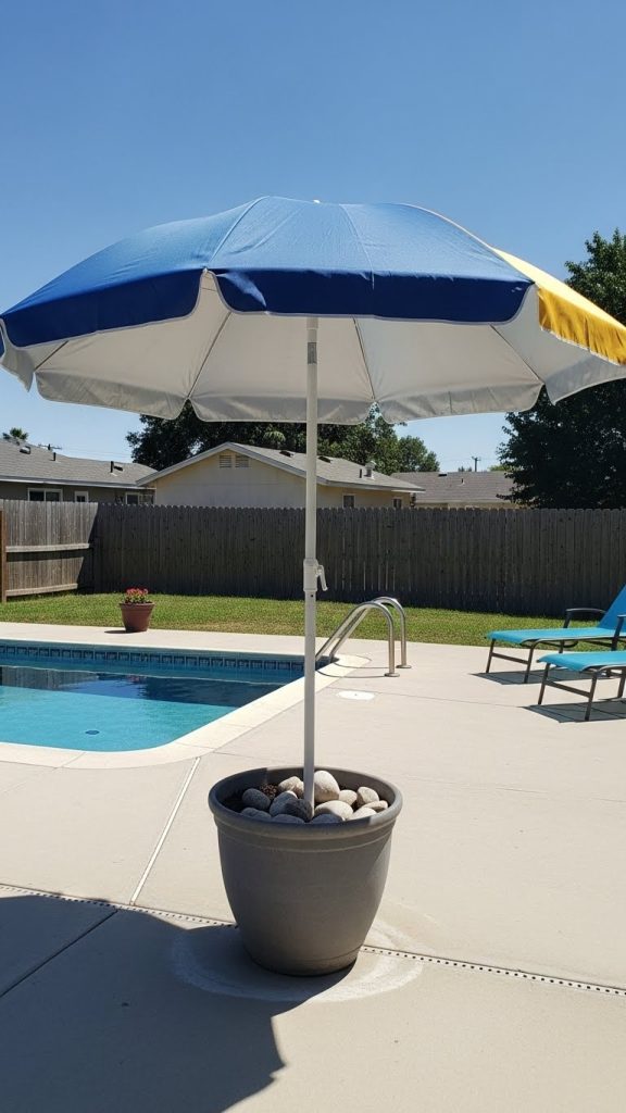 beach umbrella in a large planter pot with rocks and sand